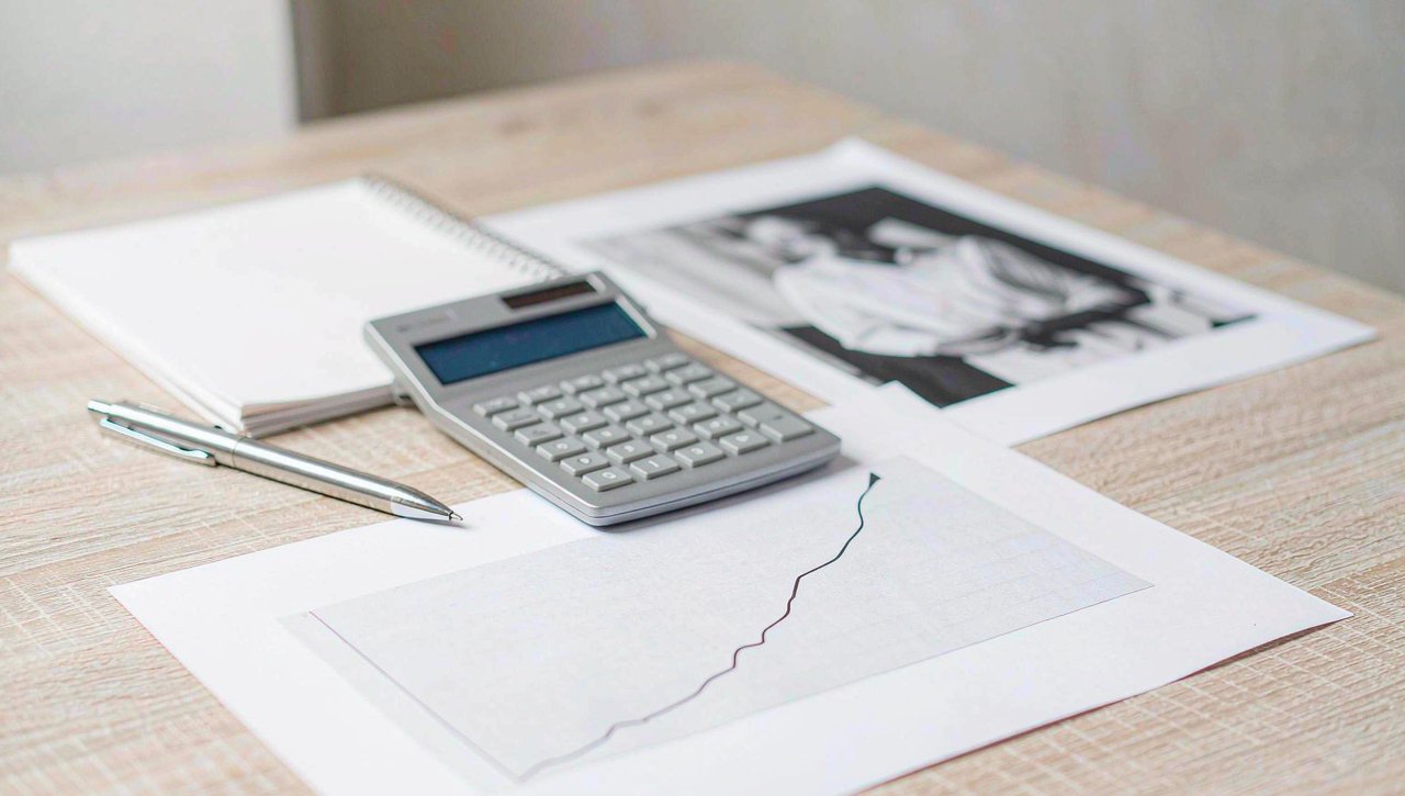 A calculator, printed yield curve charts and a notebook on a neutral desk in soft natural light
