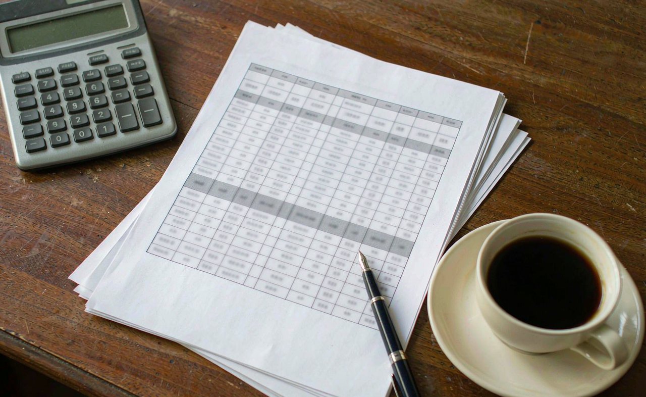 A wooden desk with a calculator, a printed yield table and a cup of black coffee